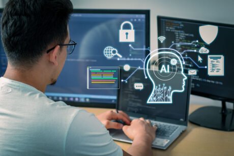 Man working on a laptop with multiple monitors showing code, while a glowing AI graphic overlay illustrates a human head with circuits and technology icons such as lock, globe, document, and chat.